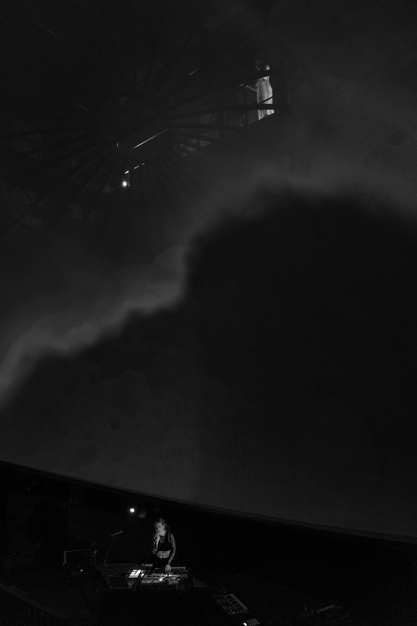 Black and white photo of the dark dome at Wisdome Malmö, with Loljud small at her instruments below