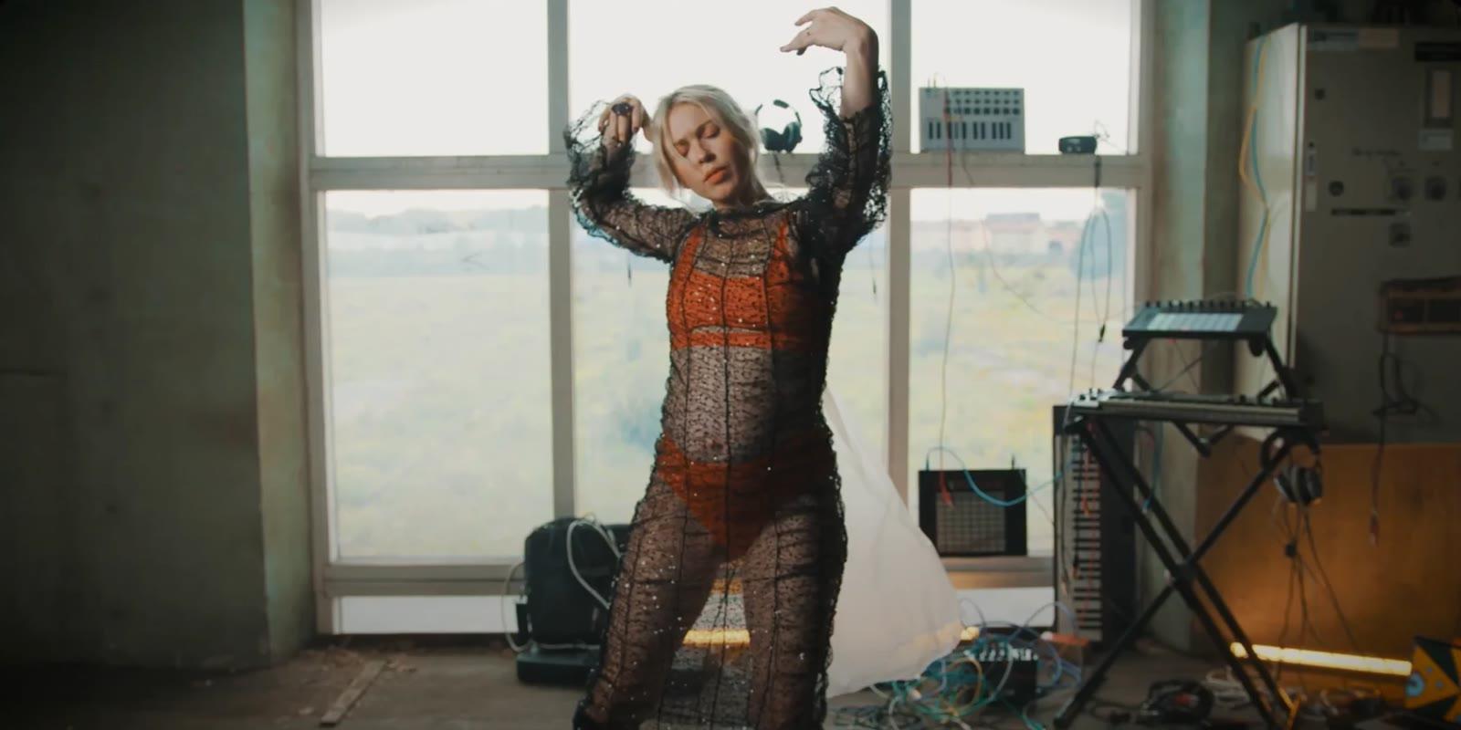 Loljud dancing in front of a window, with synthesizers and cables around her