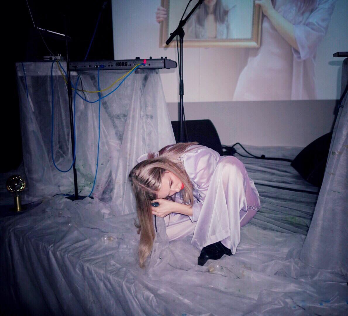 Loljud crouching on a stage draped in white plastic, singing into a microphone