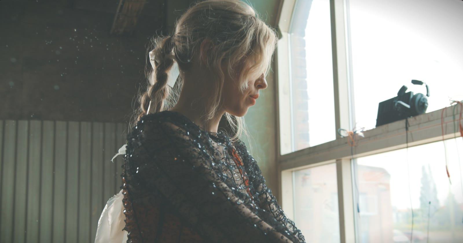 Loljud (Lotta Fahlén) in profile by a large window, in a black sequinned dress
